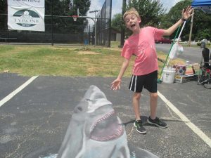 A cute child poses with a 3D chalk drawing of a shark