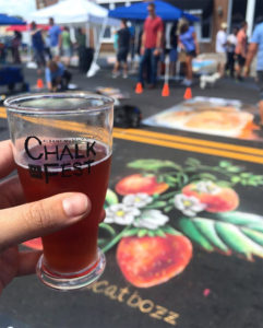 A beer held in front of a strawberry rendered in chalk on the pavement at the Albany, GA Chalk Festival.