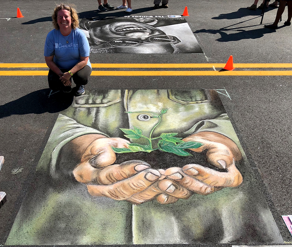 A chalk drawing of hands holding a growing tree and artist Heather Cap at the Albany Street Painting Festival.
